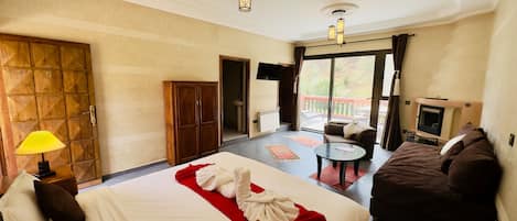 A hotel room with a large bed, a sofa, a small table, a TV, and a balcony with a view.
