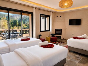 Habitación de hotel con dos camas, televisor, chimenea y balcón con mobiliario exterior.