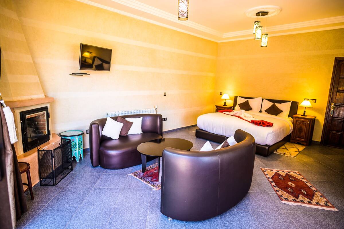 A modern hotel room with a sofa set, a bed with decorative pillows, a small table, and a fireplace.