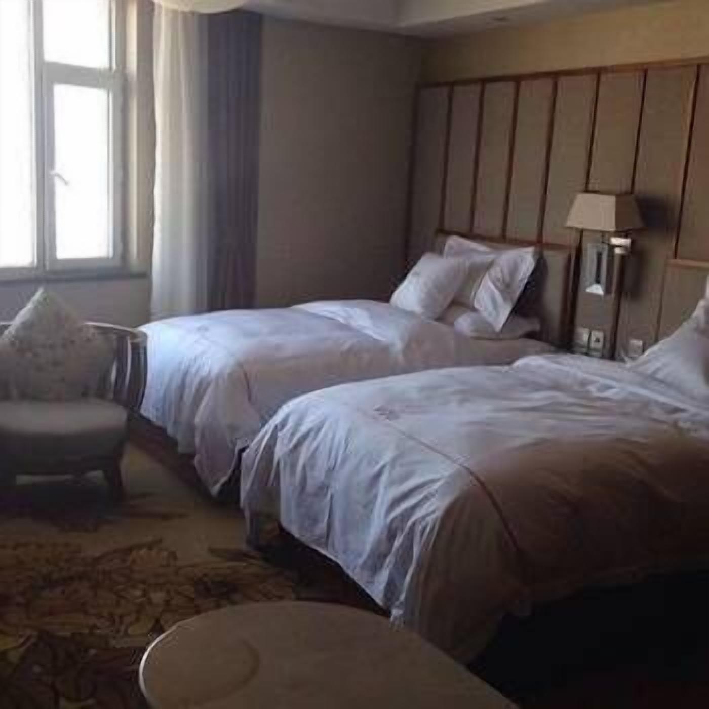 Ein Hotelzimmer mit zwei Betten, einem Sessel und einer Lampe.