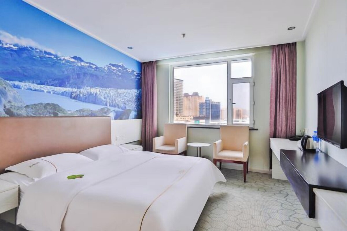 A hotel room with a large bed, a desk, a chair, a small table, and a TV.