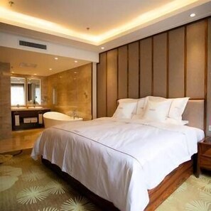 A modern bedroom with a large bed, a wooden headboard, and a bathroom with a mirror and sink. - Regent Hotel (Changchun)