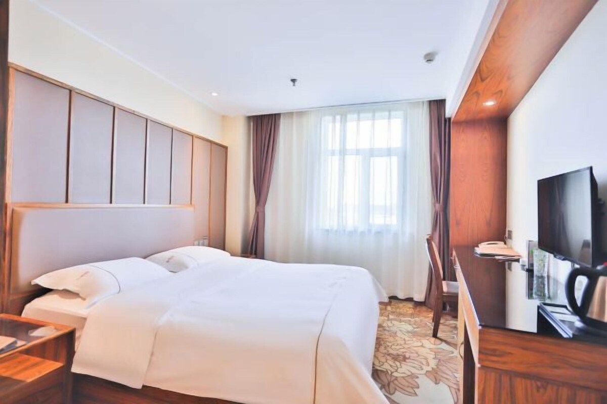 A hotel room with a bed, a desk, a television, and a window with curtains.