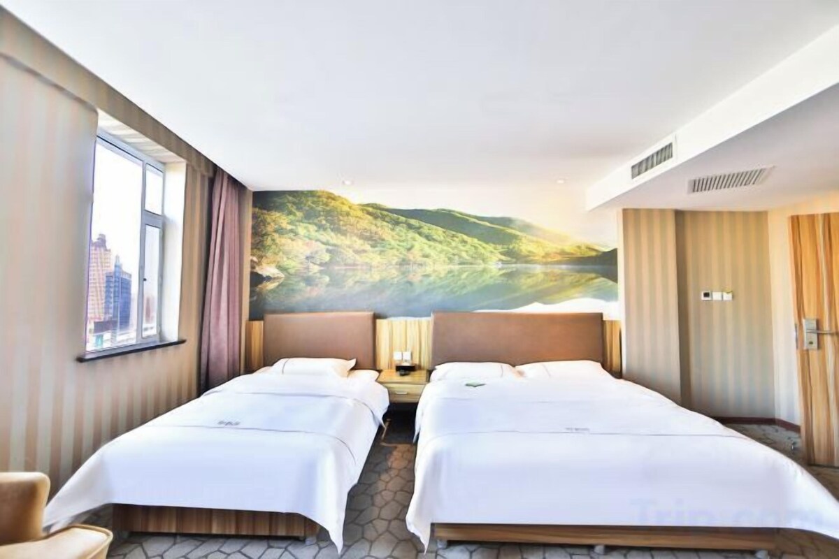 A hotel room with two beds, a window, a painting of a landscape, and a door.