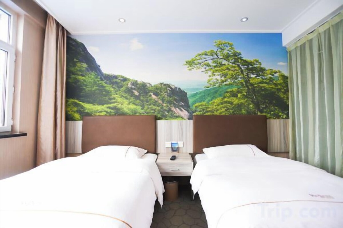 A hotel room with two beds, a desk, and a mural of a mountainous landscape.