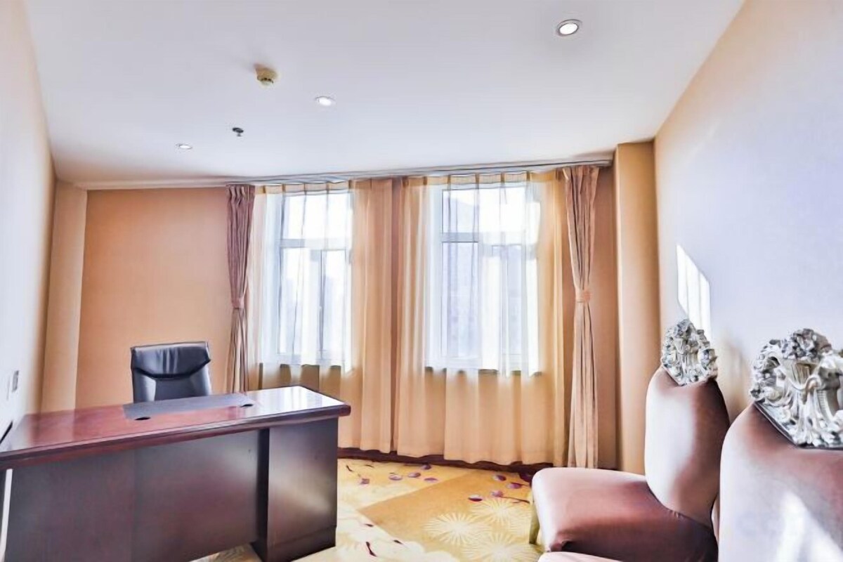 A hotel room with a desk, a chair, a sofa, and a large window with curtains.