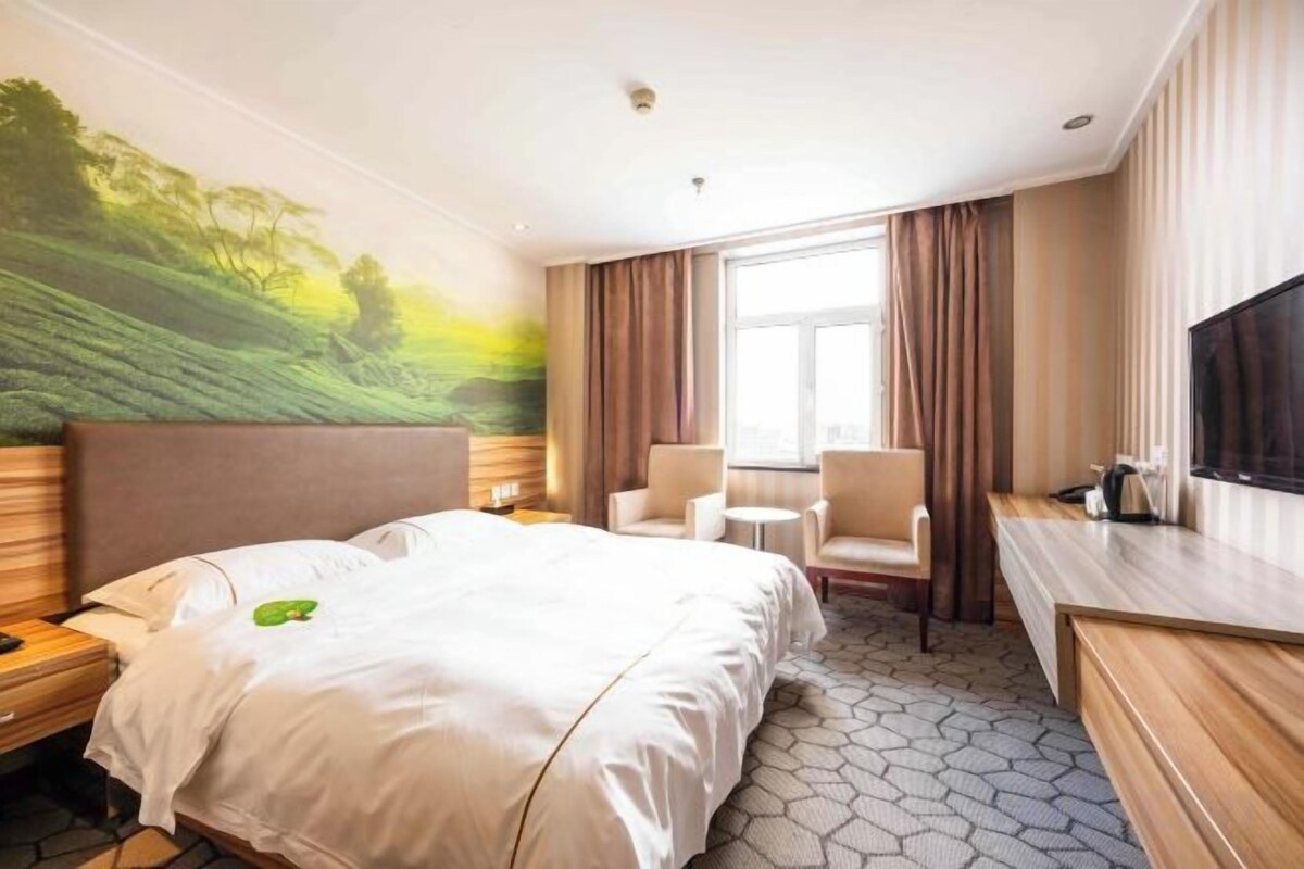 A hotel room with a bed, two chairs, a desk, a TV, and a large window.