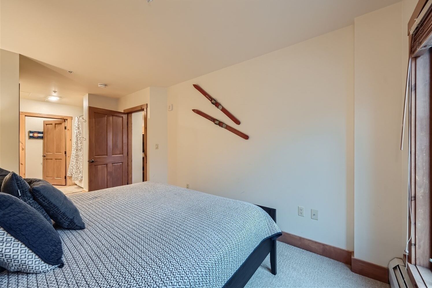 A bedroom with a bed, a wooden door, and a wall-mounted ski rack.