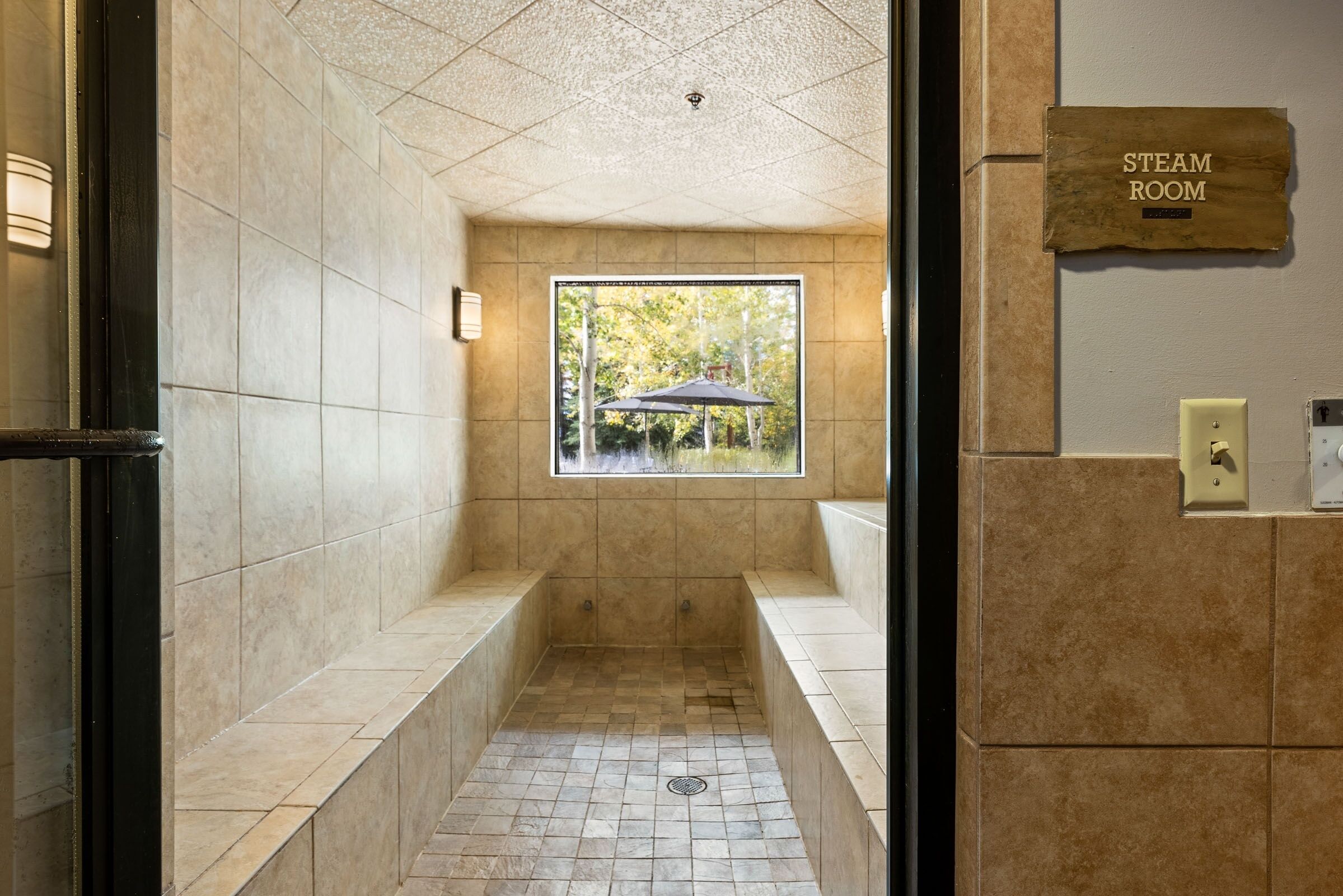 A steam room with a window view of trees, tiled walls, and a sign indicating the room's purpose.