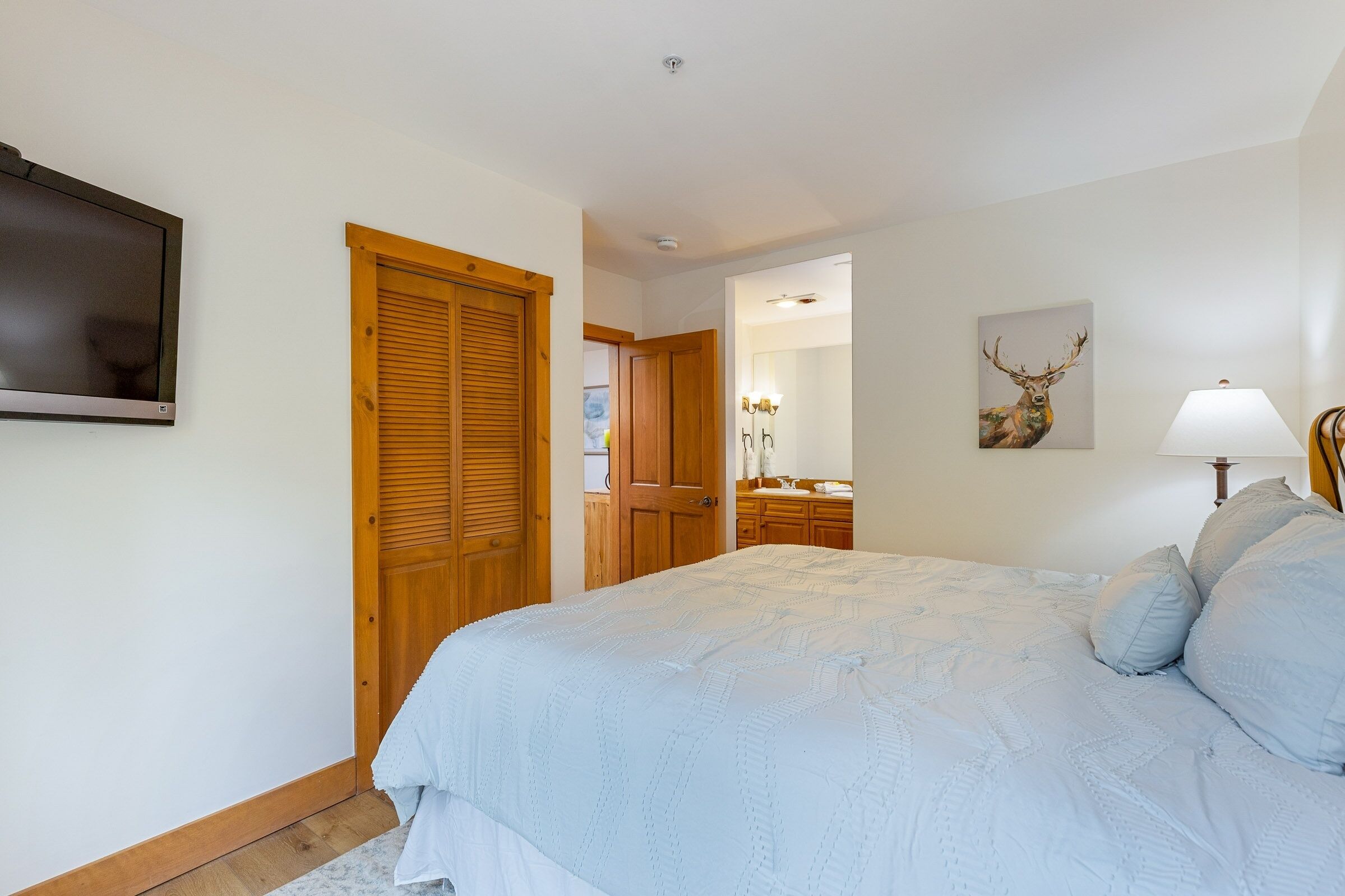 Une chambre à coucher avec un grand lit, des portes en bois, une télévision, un miroir et un tableau représentant un cerf accroché au mur.