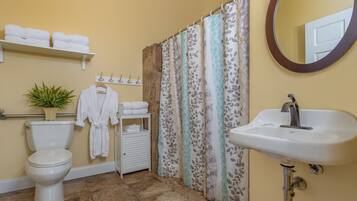 Un baño con inodoro, lavabo, cortina de ducha, espejo, toallero y estante con toallas.