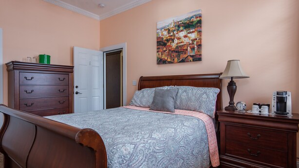 Un dormitorio con una cama de madera, una mesita de noche con lámpara, un aparador y un cuadro en la pared.