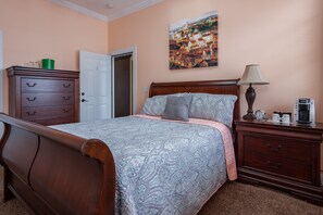 A bedroom with a wooden bed, a nightstand with a lamp, a dresser, and a painting on the wall. - Main Street Inn (Lowell)