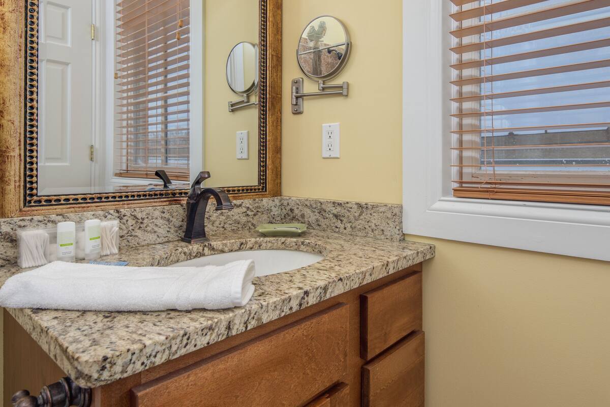 A bathroom with a granite countertop, a sink, a mirror, wooden blinds, and a towel.