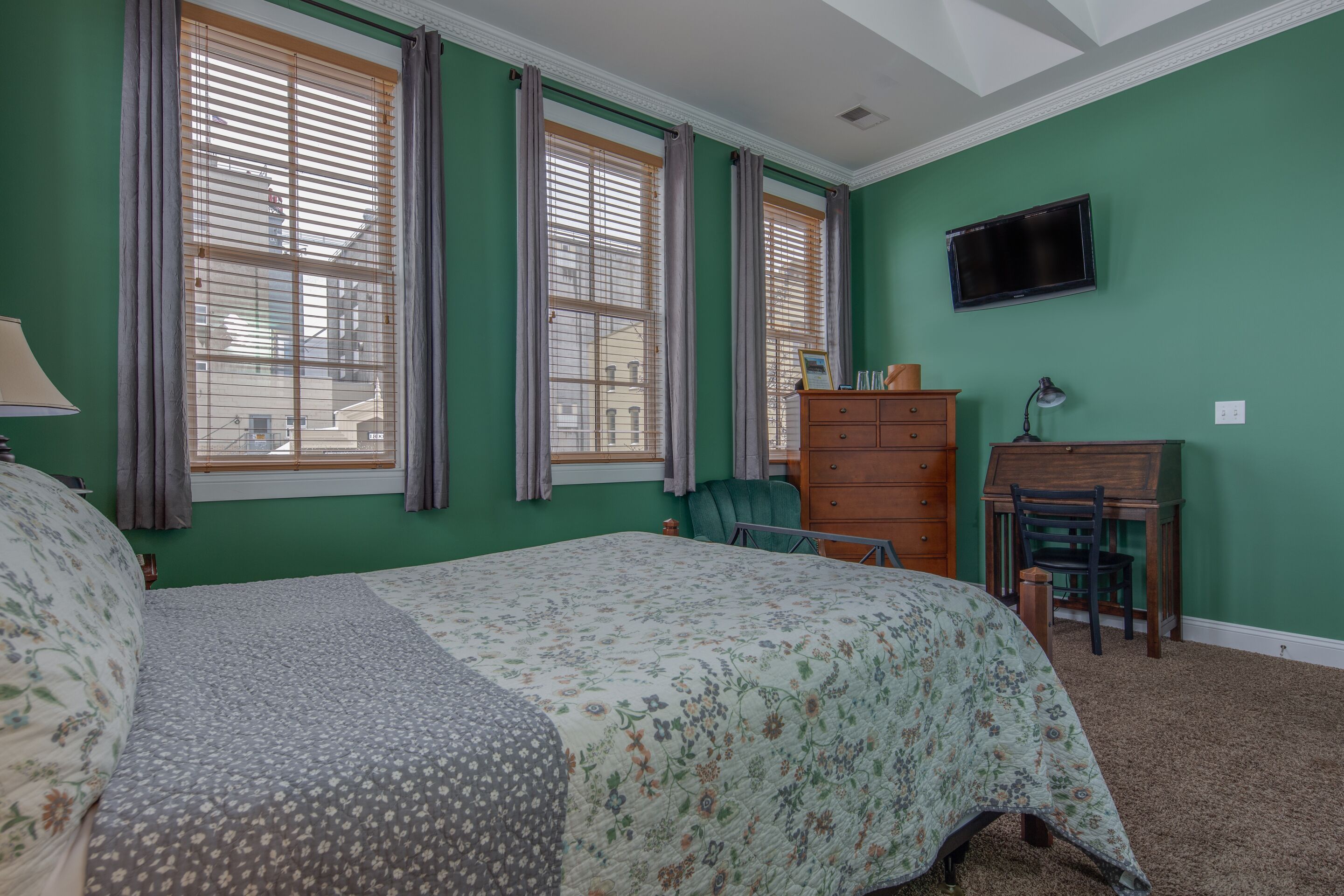 A bedroom with a bed, a dresser, a desk, and a television.