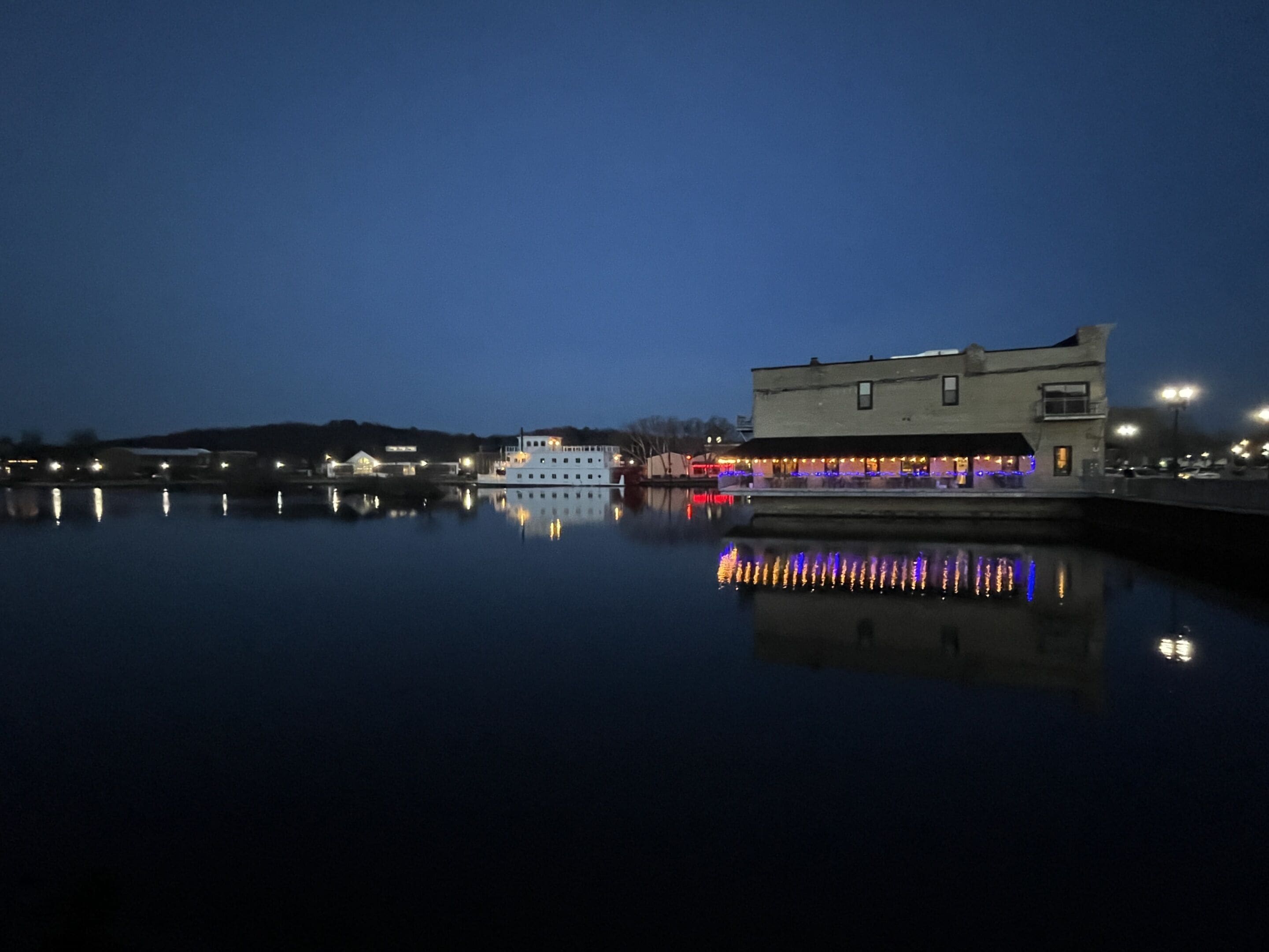 Escena costera con un edificio y un bote reflejándose en aguas tranquilas.