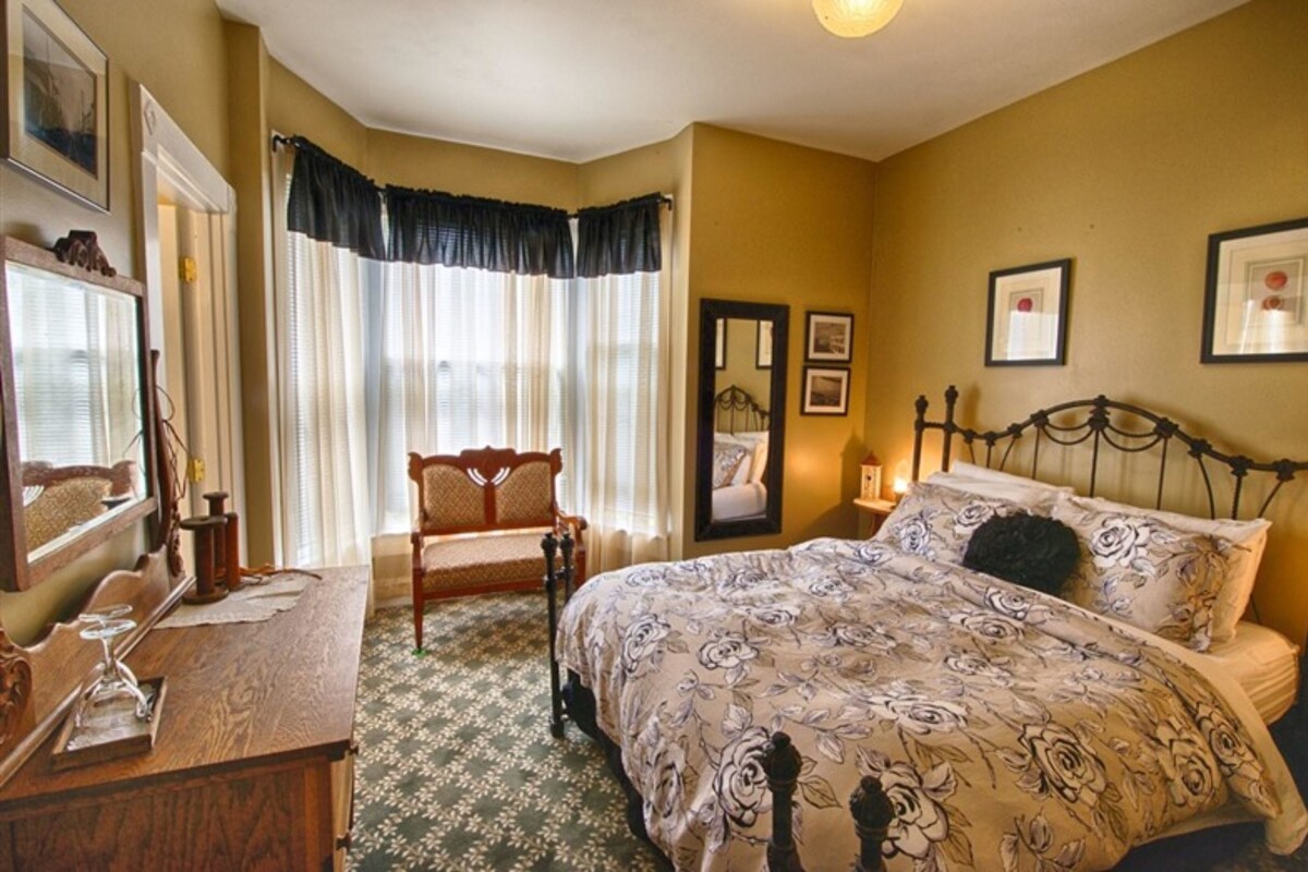 A bedroom with a bed, a chair, a desk, and a mirror.