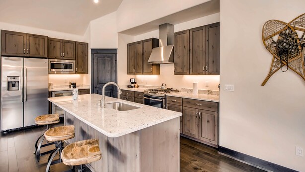 A modern kitchen with a central island, stainless steel appliances, and wooden bar stools. - River Run Townhome RR42 (Keystone)