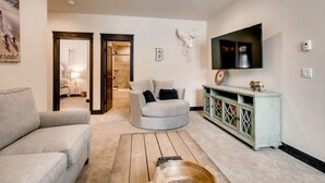 A living room with a grey sofa, a wooden coffee table, a TV mounted on the wall, and a cabinet with decorative items. - River Run Townhome RR42 (Keystone)