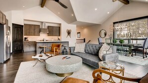 A spacious living area with a sofa, ottoman, and coffee table, a kitchen with modern appliances, and a dining area with a view of trees. - River Run Townhome RR42 (Keystone)