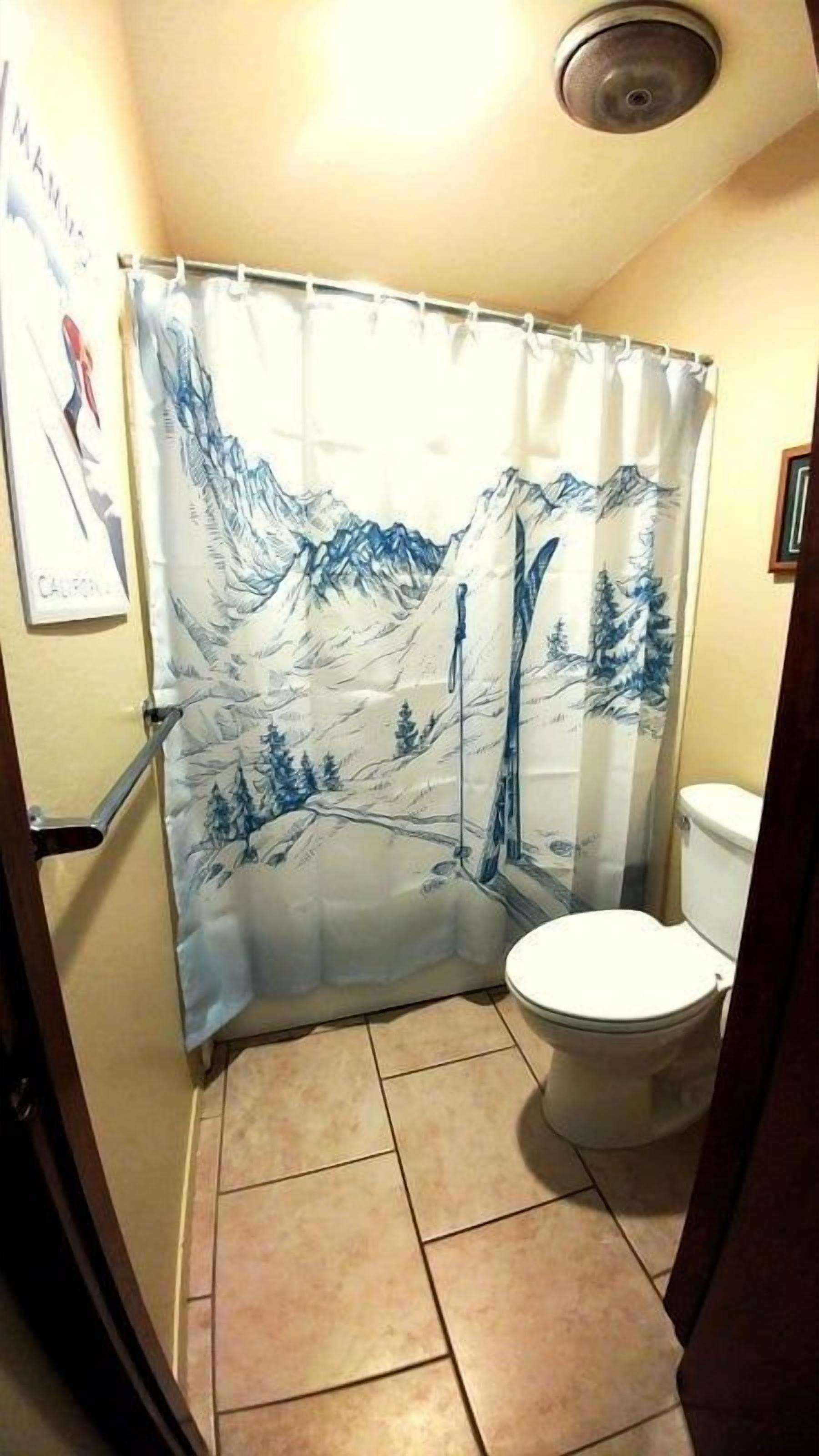 Baño con cortina de ducha que muestra un paisaje montañoso, un inodoro y suelo de baldosas.