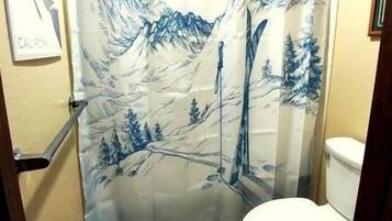 Baño con cortina de ducha que muestra un paisaje montañoso, un inodoro y suelo de baldosas.