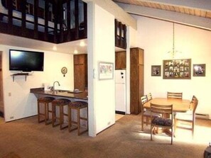 A modern kitchen with a TV, bar stools, and a dining area with a wooden table and chairs.