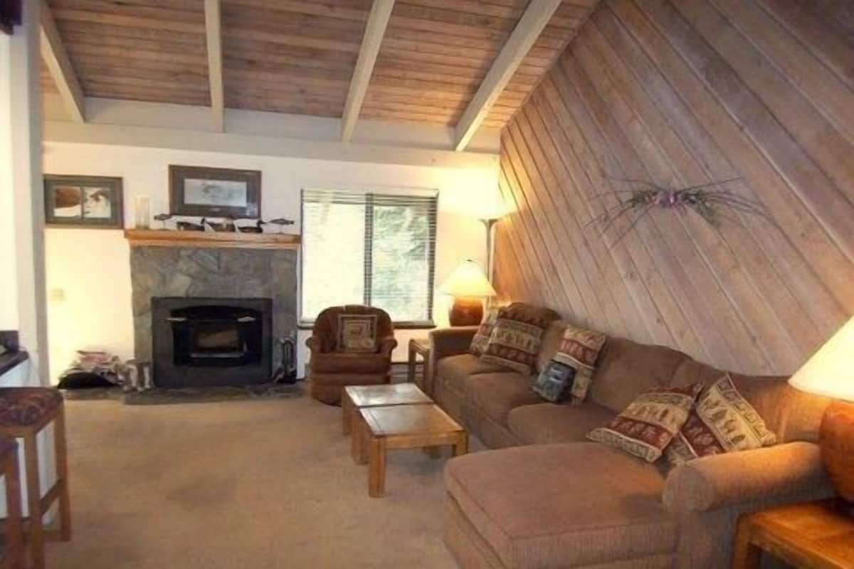 A cozy living room with a fireplace, a sofa, a coffee table, and a wooden ceiling.