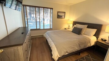 A bedroom with a bed, bedside tables, a dresser, a window with blinds, and a picture on the wall.