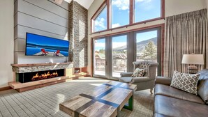 A modern living room with a fireplace, a flat-screen TV, and a large window offering a scenic view.