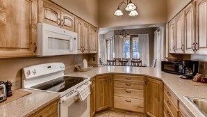 A kitchen with wooden cabinets, a white stove, and a dining area with a table and chairs. - Quicksilver 1662 (Keystone)
