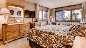 A bedroom with a large bed, a wooden dresser, a TV, and windows with curtains. - Quicksilver 1662 (Keystone)