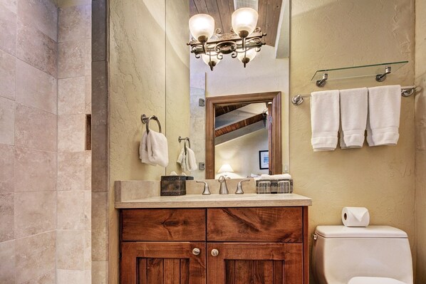 A bathroom with a wooden vanity, a white toilet, a mirror, and a chandelier.