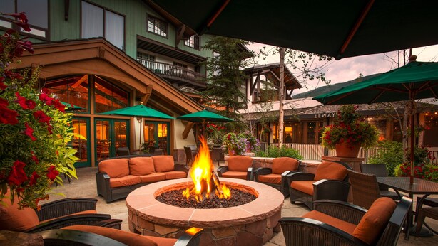 An outdoor patio with a stone fire pit surrounded by wicker furniture and green umbrellas. - Modern 2 BR Condo Lodge at Vail, Walk to Gondola by RedAwning (Vail)