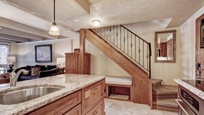 A kitchen with granite countertops, wooden cabinets, a stainless steel sink, a built-in oven, and a wooden staircase with a black railing. - Modern 2 BR Condo Lodge at Vail, Walk to Gondola by RedAwning (Vail)