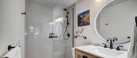 A modern bathroom with a glass-enclosed shower, a white toilet, and a wooden vanity with a large mirror.