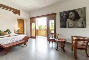 Una habitación de hotel con cama, un banco, una mesa con un florero y un cuadro en la pared.
