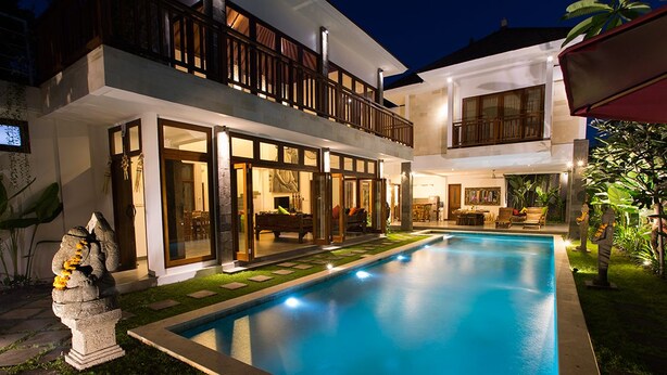 Uma casa de dois andares com piscina, janelas amplas e varanda.