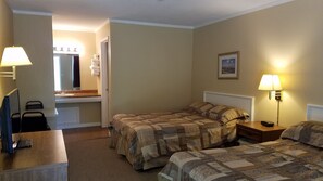 A hotel room with two beds, a desk, a chair, a lamp, and a painting on the wall.