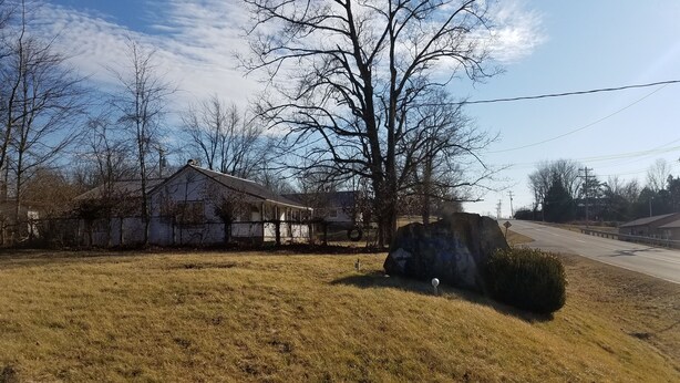 A rural setting with a house, a large rock, and a grassy area.