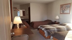 A hotel room with a bed, a desk with a lamp, a chair, and a wardrobe.