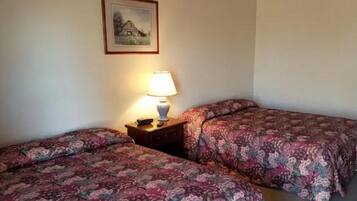 A room with two beds, each with floral-patterned bedding, a nightstand with a lamp, and a framed picture on the wall.