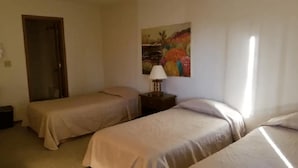 A room with two single beds, a nightstand with a lamp, a painting on the wall, and a door.