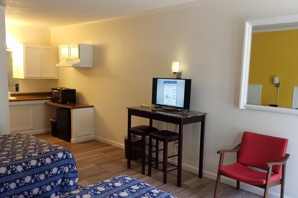 Habitación compacta con cama, escritorio con computadora, silla y kitchenette.