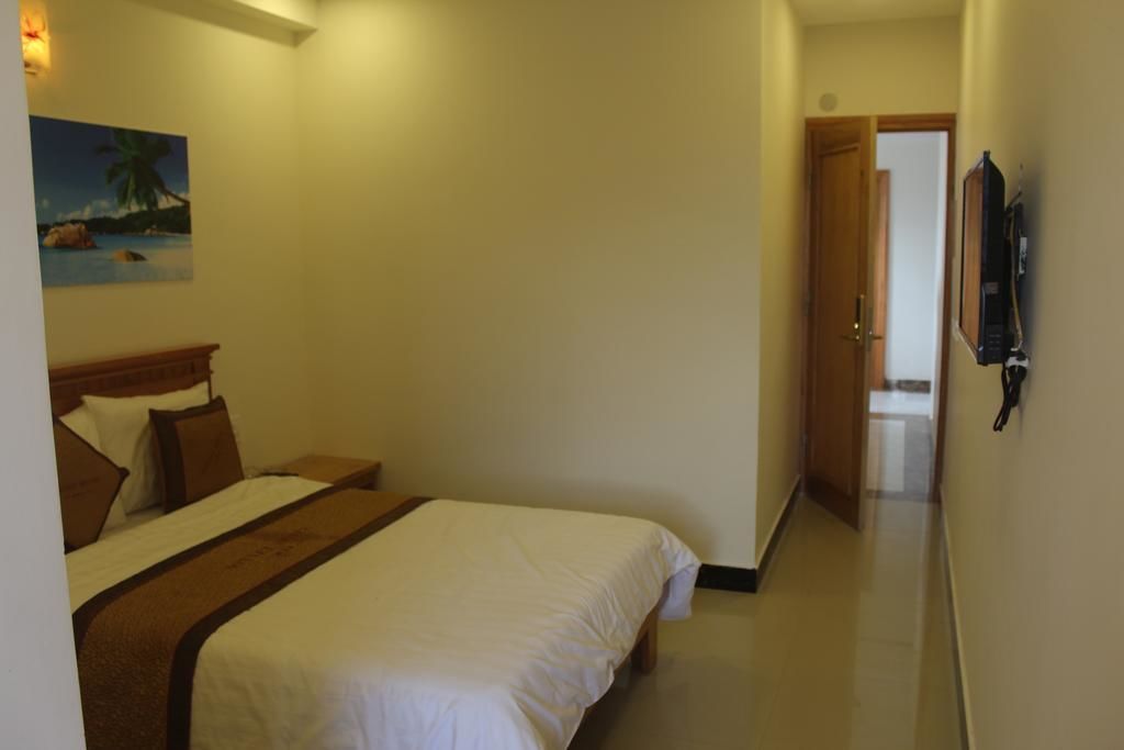 Ein Hotelzimmer mit Bett, einem Bild mit tropischer Szenerie und einem Fernseher an der Wand.