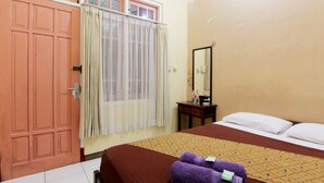 A hotel room with a bed, a wooden nightstand, a mirror, and a window with curtains.