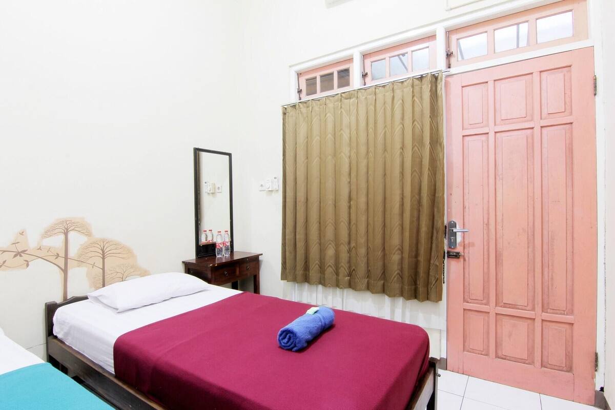 Un dormitorio con una cama, un aparador de madera, un espejo, una ventana con cortinas y una puerta rosa.