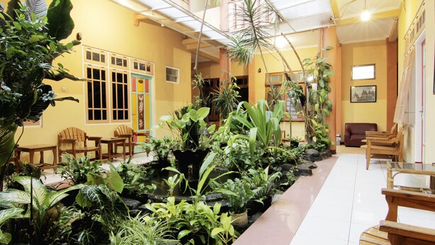 A lobby with a long bench, wooden chairs, and a variety of potted plants.