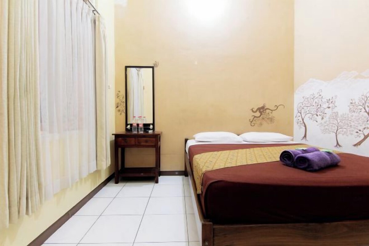 Une chambre d’hôtel avec un lit, une table de chevet, un miroir et un mur décoré d’une fresque représentant un arbre.