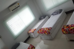 A room with three single beds, each with a colorful floral bedspread. There is a window with blinds on the left, and an air conditioning unit mounted on the wall above the beds. - H Youth Hostel (Bangkok)
